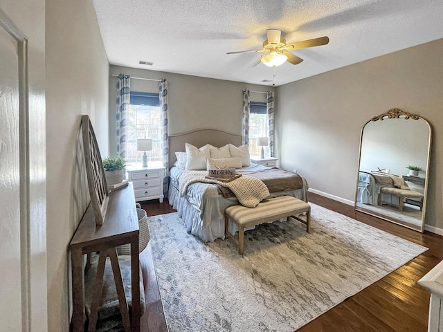 bedroom featuring visible vents, a textured ceiling, wood finished floors, baseboards, and ceiling fan