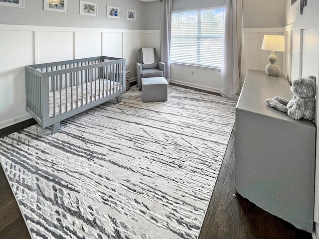 bedroom with a nursery area, wainscoting, and a decorative wall