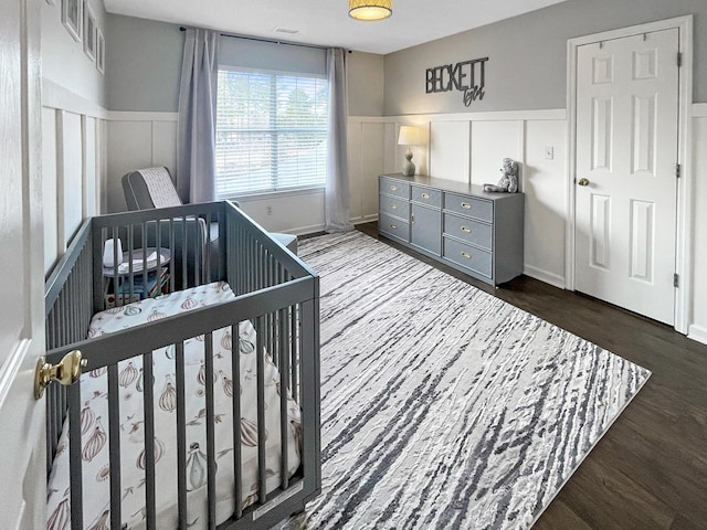 bedroom with a wainscoted wall, dark wood-style floors, and a decorative wall