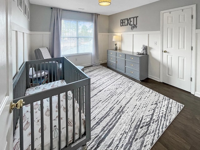 bedroom with a decorative wall, a wainscoted wall, and dark wood-style flooring