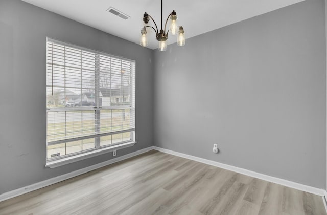 spare room with light wood-style floors, baseboards, visible vents, and a chandelier