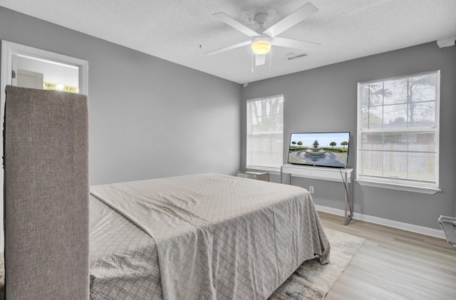 bedroom featuring a textured ceiling, ceiling fan, visible vents, baseboards, and light wood finished floors