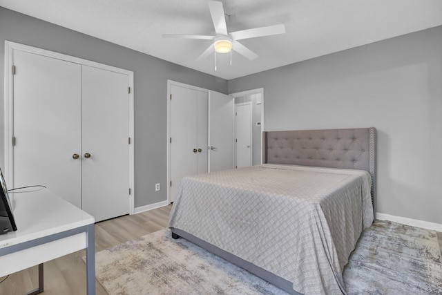 bedroom featuring a ceiling fan, light wood-type flooring, baseboards, and two closets