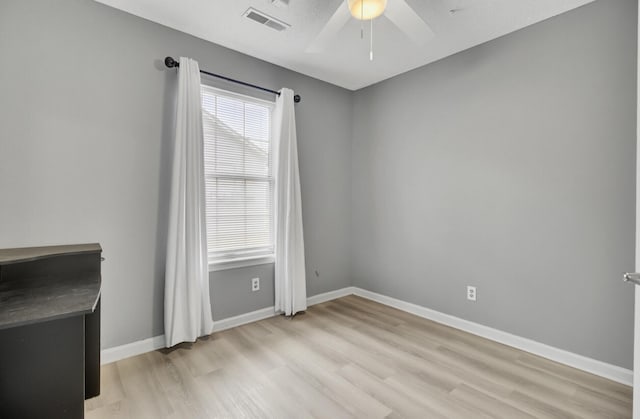 empty room featuring light wood-style floors, a ceiling fan, visible vents, and baseboards