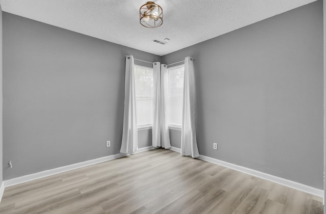 unfurnished room with a textured ceiling, light wood-style flooring, visible vents, and baseboards