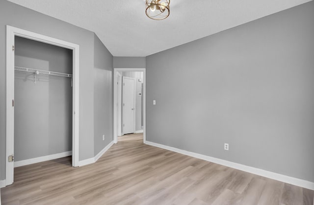 unfurnished bedroom featuring a closet, light wood-style flooring, baseboards, and a textured ceiling