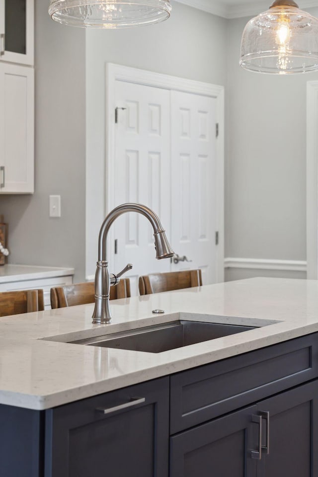 kitchen with hanging light fixtures, light stone countertops, gray cabinets, and a sink