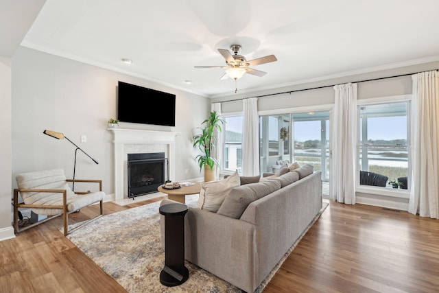 living room with baseboards, a fireplace with flush hearth, ceiling fan, crown molding, and light wood-type flooring