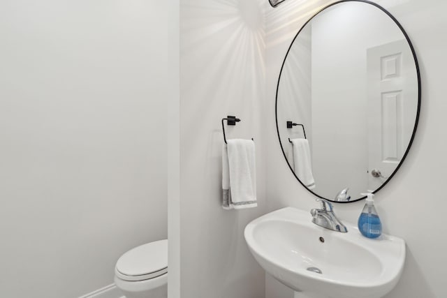 half bath with baseboards, a sink, and toilet