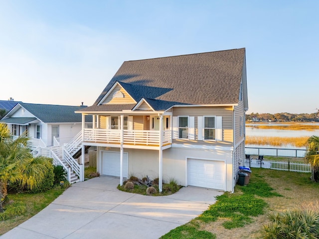 beach home with an attached garage, roof with shingles, a water view, and stucco siding