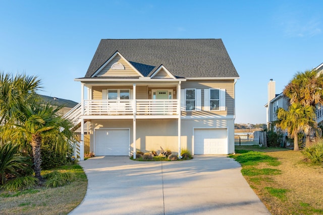 coastal home featuring a garage, concrete driveway, roof with shingles, and fence