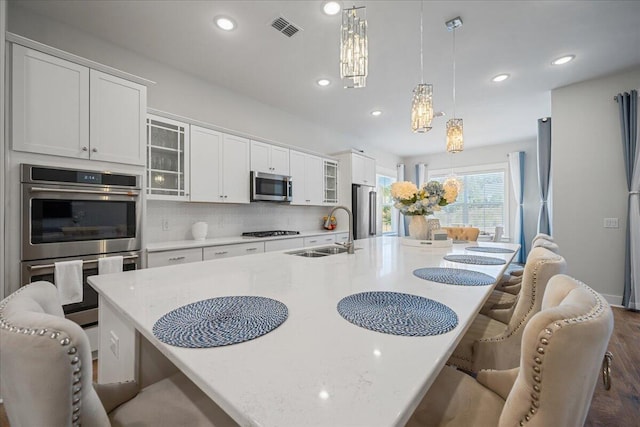 kitchen featuring sink, stainless steel appliances, a kitchen island with sink, and hanging light fixtures