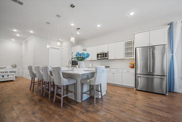 kitchen featuring decorative light fixtures, white cabinetry, a kitchen breakfast bar, a center island with sink, and appliances with stainless steel finishes