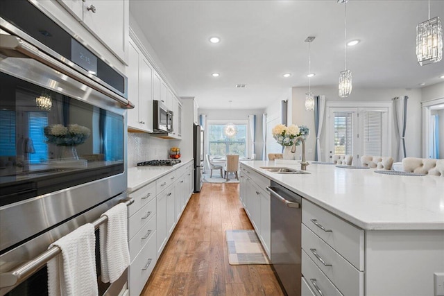 kitchen with sink, white cabinets, a center island with sink, pendant lighting, and appliances with stainless steel finishes