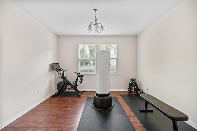 workout area featuring a chandelier, dark wood-style floors, and baseboards