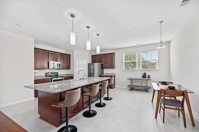 kitchen with appliances with stainless steel finishes, a breakfast bar, baseboards, an island with sink, and dark brown cabinets
