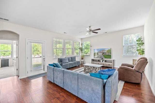 living area with dark wood finished floors, ceiling fan, arched walkways, and healthy amount of natural light
