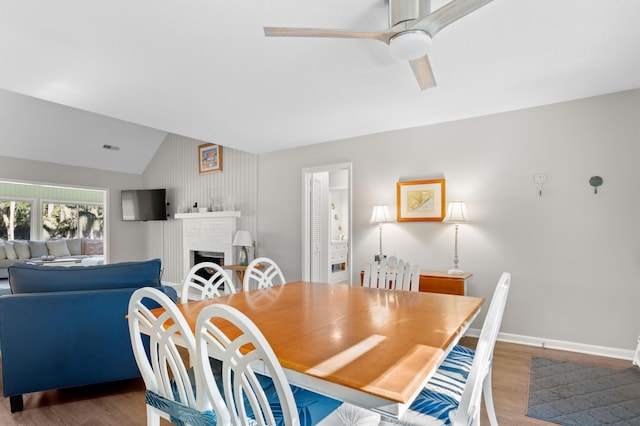 dining space featuring lofted ceiling, a brick fireplace, hardwood / wood-style floors, and ceiling fan