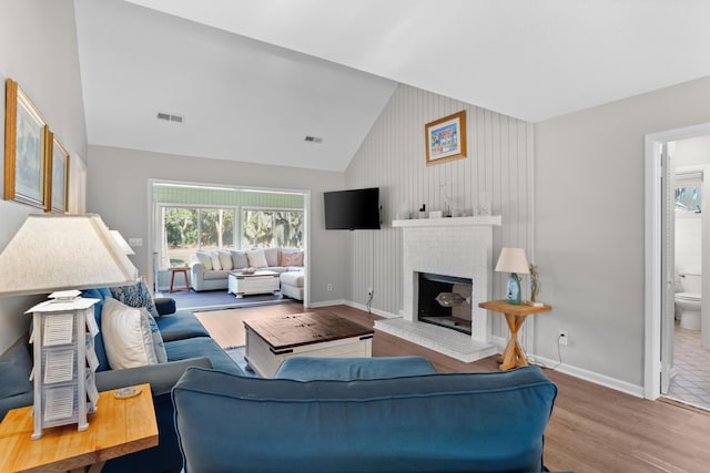 living room featuring high vaulted ceiling, a fireplace, and light hardwood / wood-style flooring