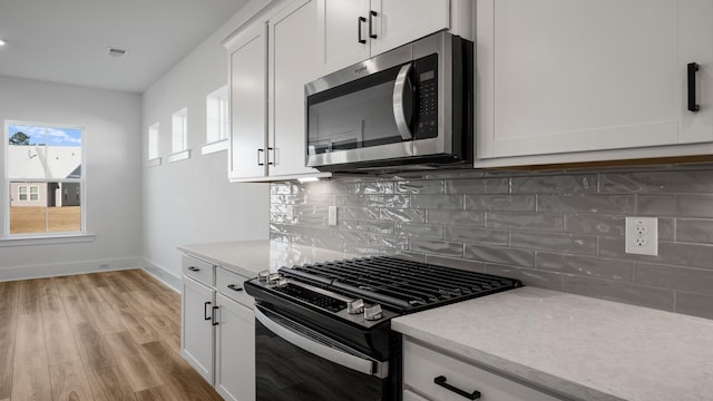 kitchen featuring stainless steel microwave, white cabinetry, light wood-style floors, backsplash, and gas range oven