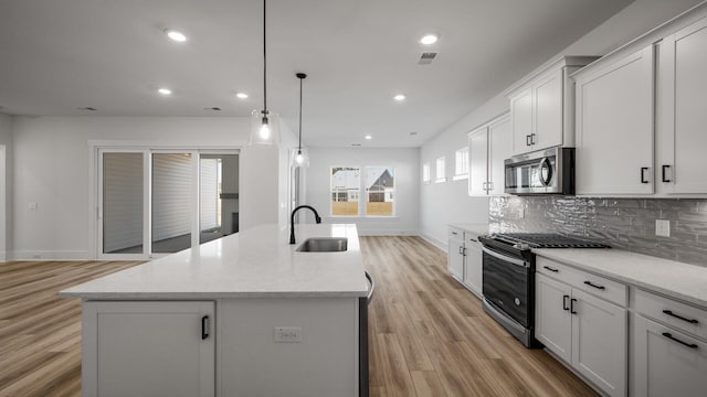 kitchen with range with gas cooktop, a center island with sink, stainless steel microwave, decorative backsplash, and a sink