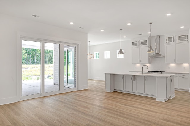 kitchen featuring a healthy amount of sunlight, wall chimney exhaust hood, an island with sink, and white cabinets