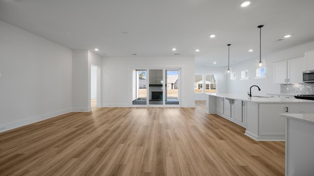 unfurnished living room featuring baseboards, recessed lighting, a sink, and light wood-style floors