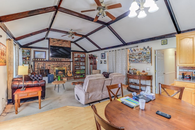 dining area featuring ceiling fan with notable chandelier, lofted ceiling with beams, a fireplace, and light hardwood / wood-style floors