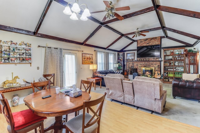 dining space with ceiling fan with notable chandelier, hardwood / wood-style flooring, a fireplace, and vaulted ceiling with beams