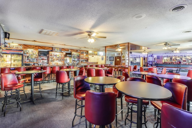 dining area with bar, ceiling fan, dark carpet, and a textured ceiling