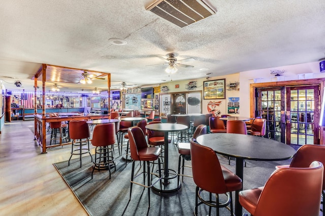 dining room with a textured ceiling, ceiling fan, and bar area