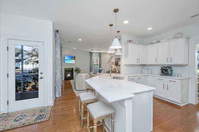 kitchen featuring a glass covered fireplace, a peninsula, light wood-style flooring, and a sink