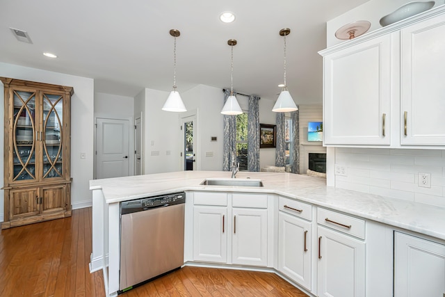 kitchen featuring visible vents, a peninsula, stainless steel dishwasher, light wood-style floors, and a sink