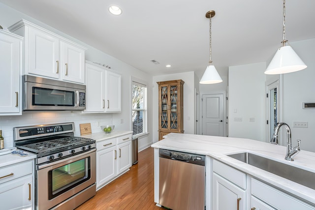 kitchen featuring light wood finished floors, backsplash, appliances with stainless steel finishes, white cabinetry, and a sink