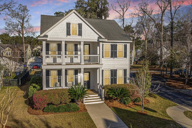 view of front of house with a balcony, a shingled roof, a front lawn, and fence