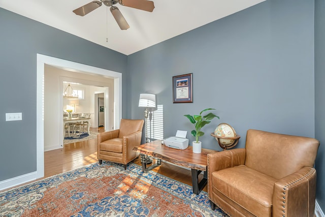 living area featuring baseboards, ceiling fan, and wood finished floors