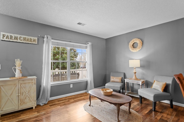 living area with baseboards, a textured ceiling, visible vents, and wood finished floors