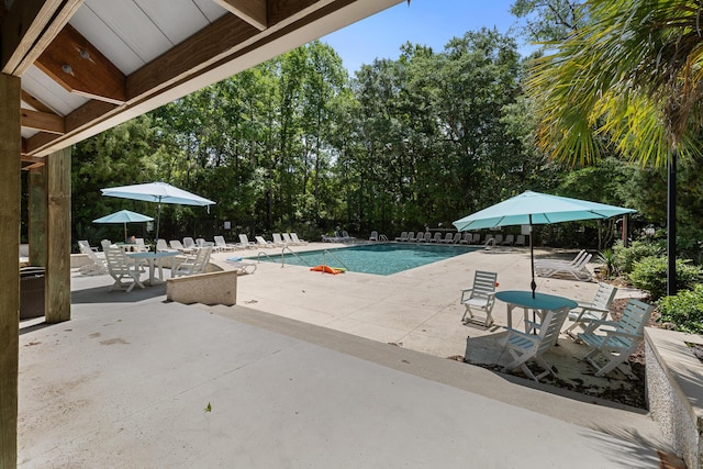 community pool featuring a patio, fence, and view of wooded area