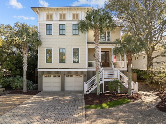 beach home with decorative driveway, a porch, stairway, french doors, and an attached garage