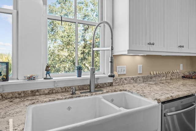 interior details with a sink, light stone counters, stainless steel dishwasher, and white cabinets