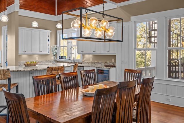 dining area with a chandelier, wine cooler, wood finished floors, and wainscoting