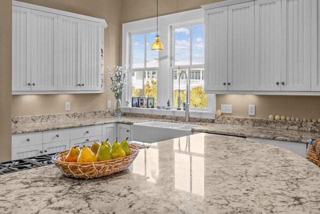 kitchen featuring hanging light fixtures, white cabinets, light stone countertops, and a sink