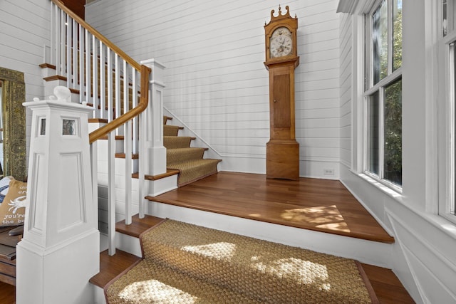 stairway with wooden walls, a healthy amount of sunlight, and wood finished floors