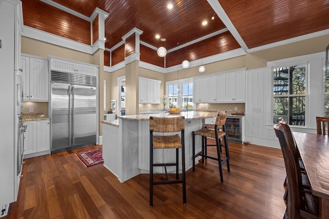 kitchen with dark wood-type flooring, stainless steel built in refrigerator, a center island, white cabinets, and wood ceiling