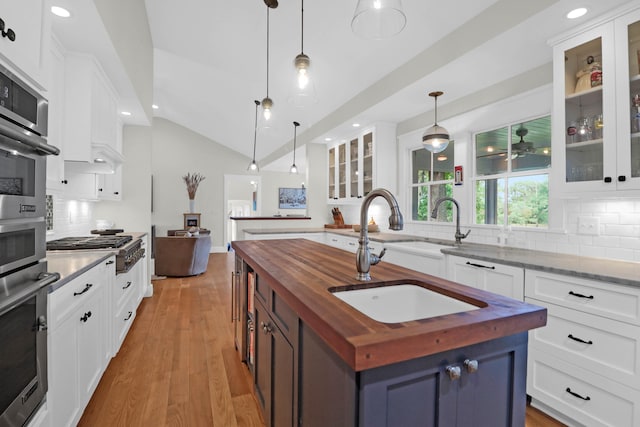 kitchen featuring white cabinetry, decorative light fixtures, an island with sink, and wooden counters