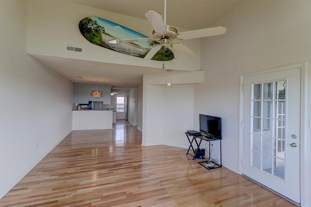 unfurnished living room with ceiling fan, a towering ceiling, and light hardwood / wood-style flooring