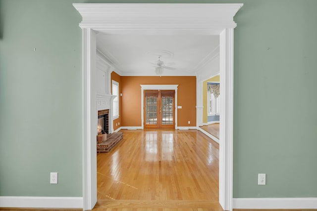 interior space featuring french doors, light wood finished floors, ornamental molding, a brick fireplace, and baseboards