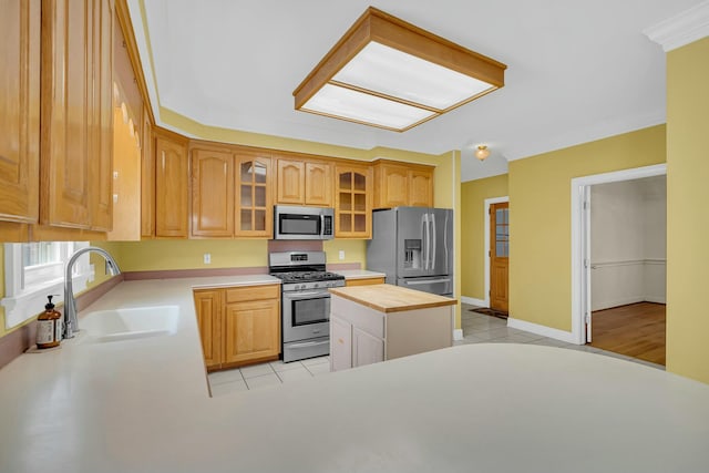 kitchen featuring light tile patterned floors, baseboards, glass insert cabinets, appliances with stainless steel finishes, and a sink