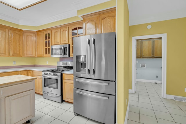 kitchen with light tile patterned floors, appliances with stainless steel finishes, ornamental molding, and glass insert cabinets