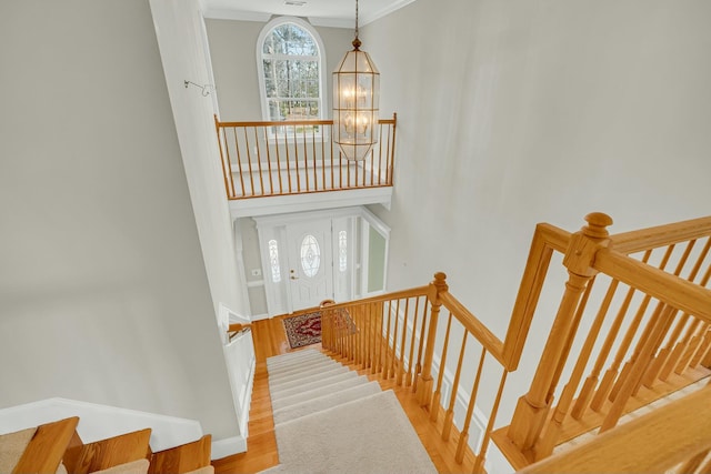 staircase featuring baseboards, a towering ceiling, ornamental molding, wood finished floors, and a notable chandelier